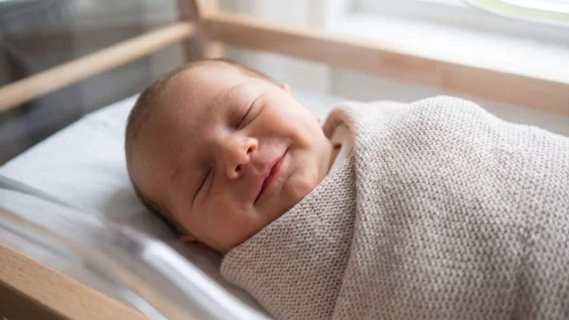 Newborn baby smiling peacefully in sleep, illustrating a normal reflex smile rather than an emotional expression.
