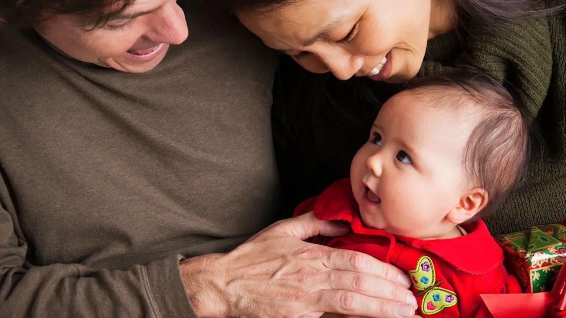 Parents holding smiling baby in red outfit with butterfly.