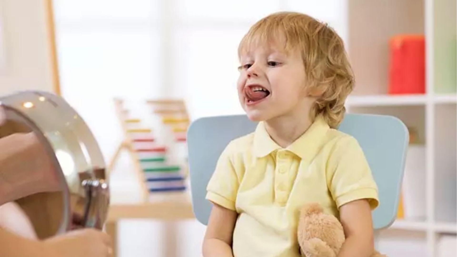 Toddler sticking tongue out in mirror during therapy for excessive drooling.