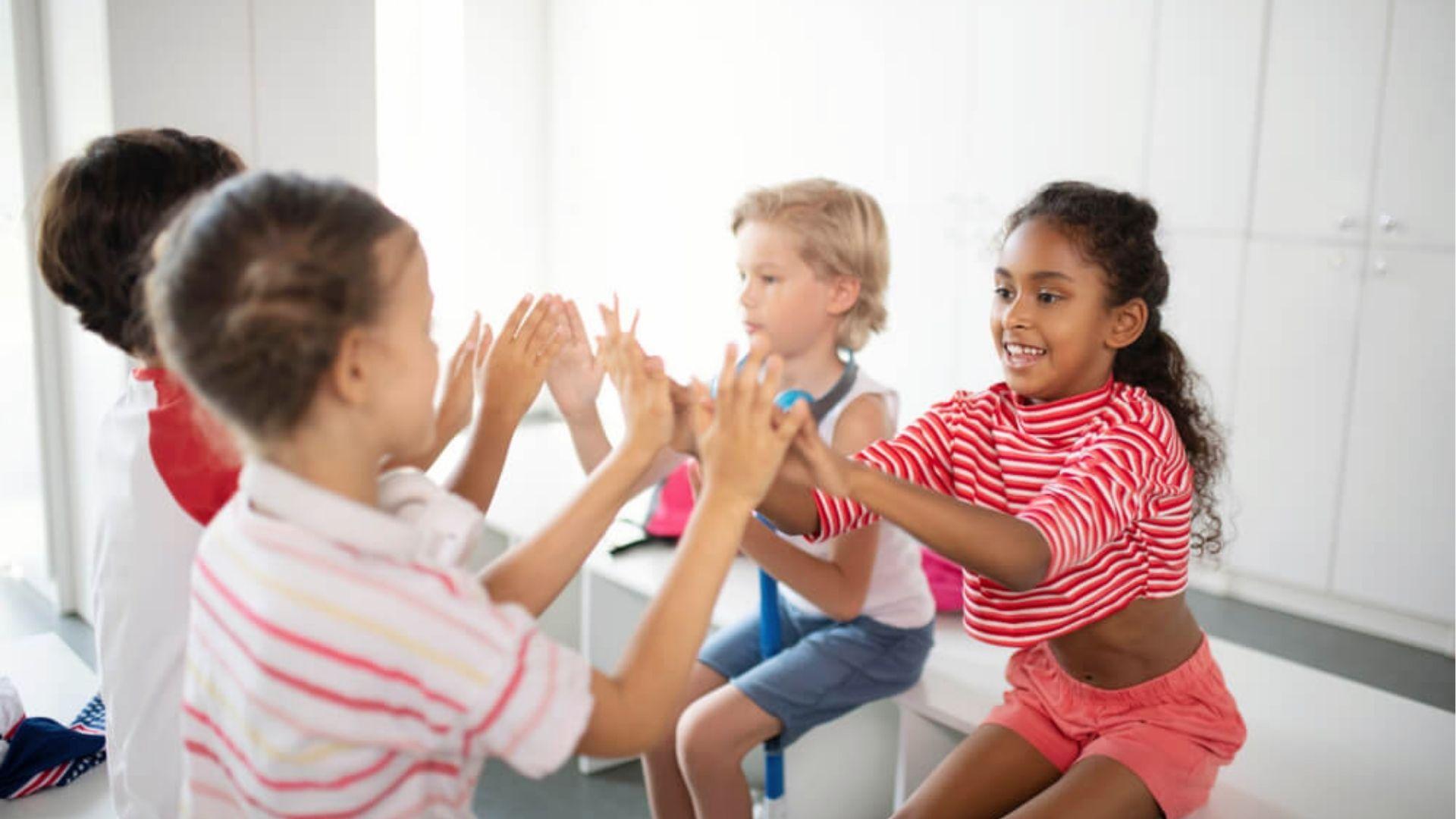 Four kids sitting indoors playing a hand-clapping game together.