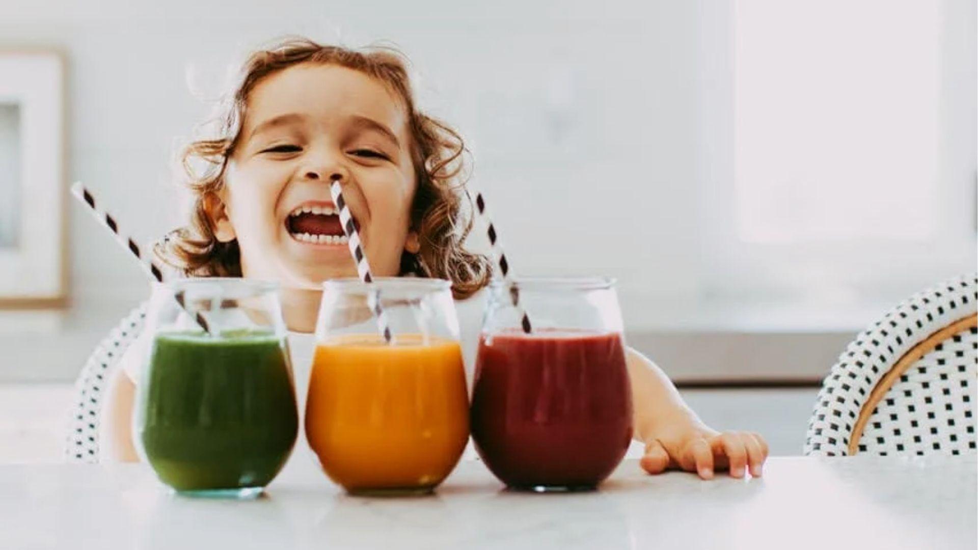 Happy child laughing behind three colorful healthy juices green, orange, beetroot.