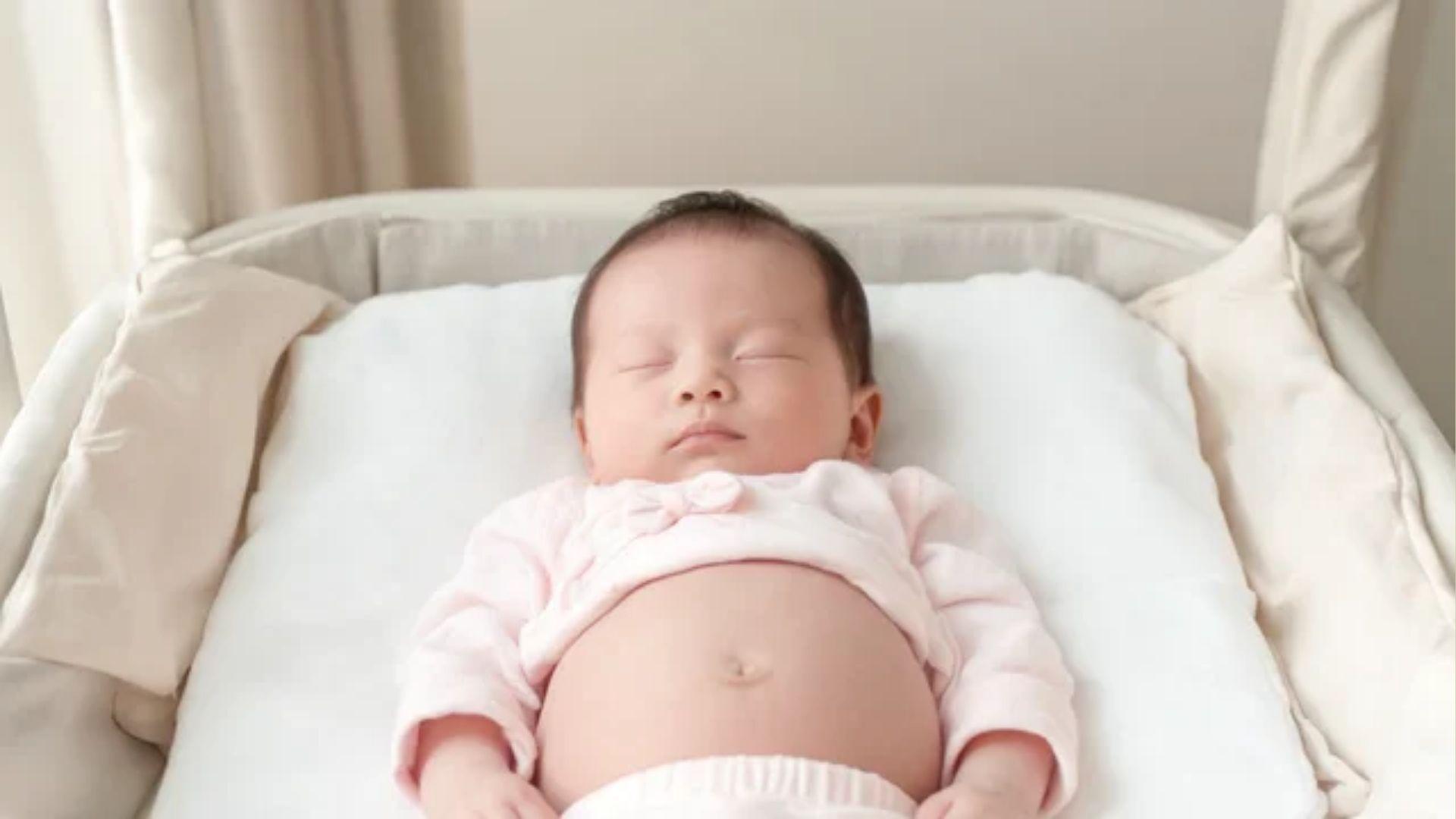 Newborn baby lying on their back in a bassinet with the abdomen visible