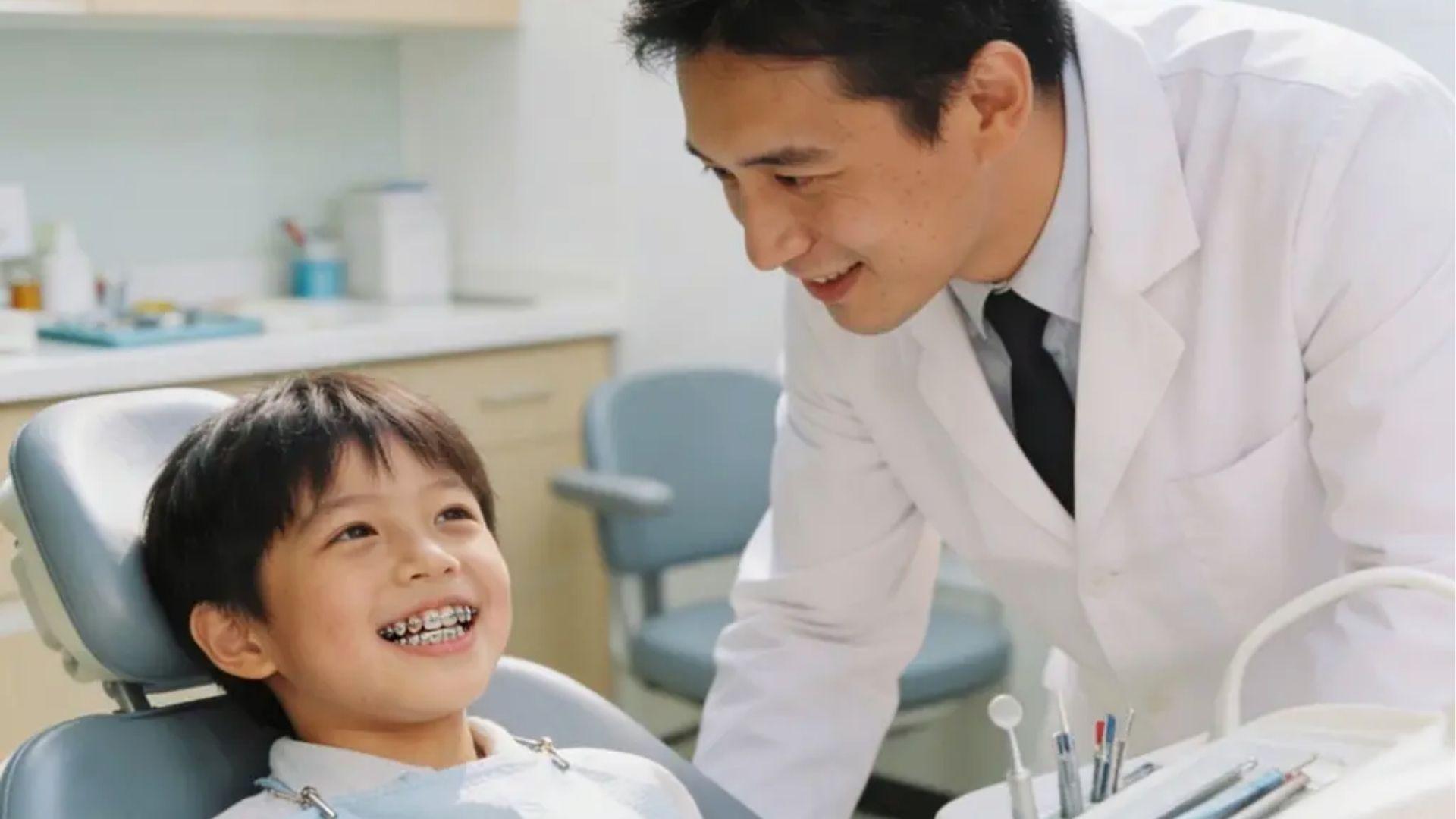 Happy young boy with braces smiling in dental chair with dentist during orthodontic checkup.