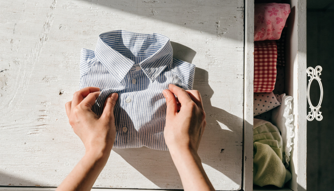 Person holding pink butterfly baby dress beside stacked folded baby clothes.