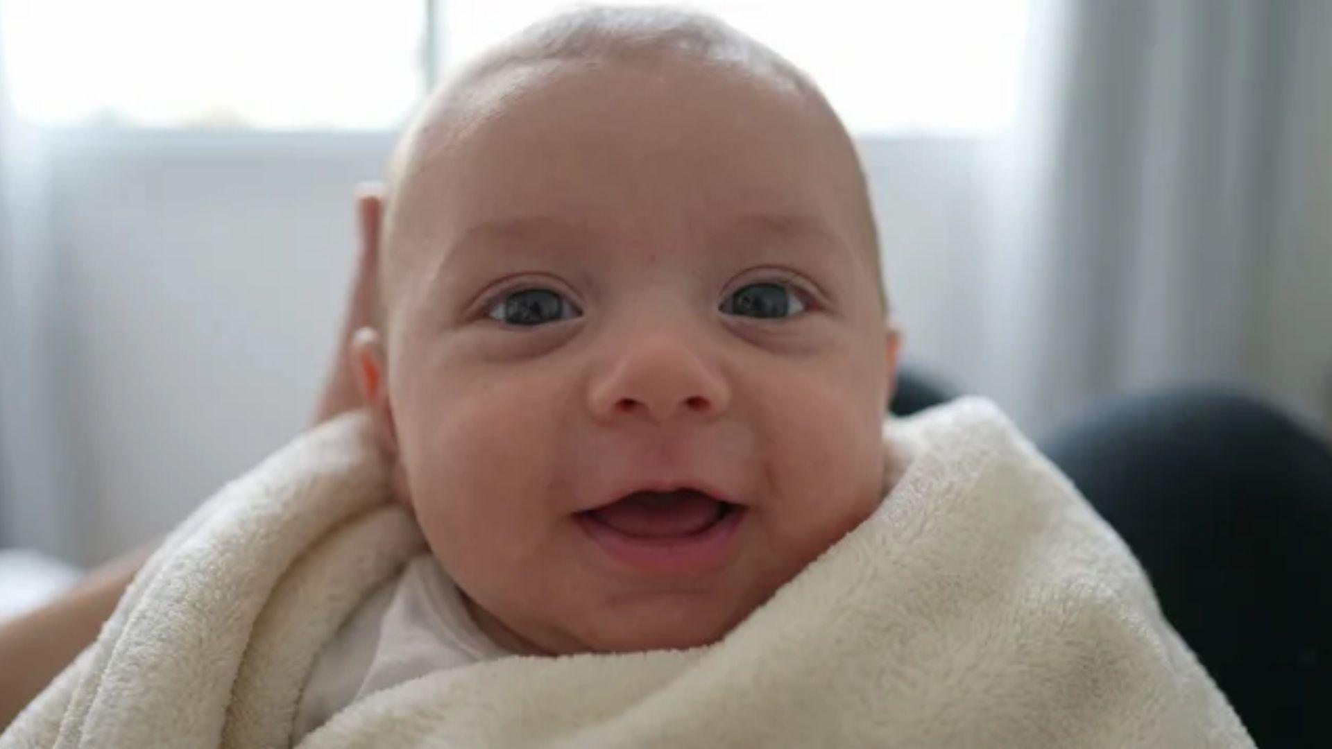Infant making eye contact with a nearby face while smiling and opening the mouth to coo