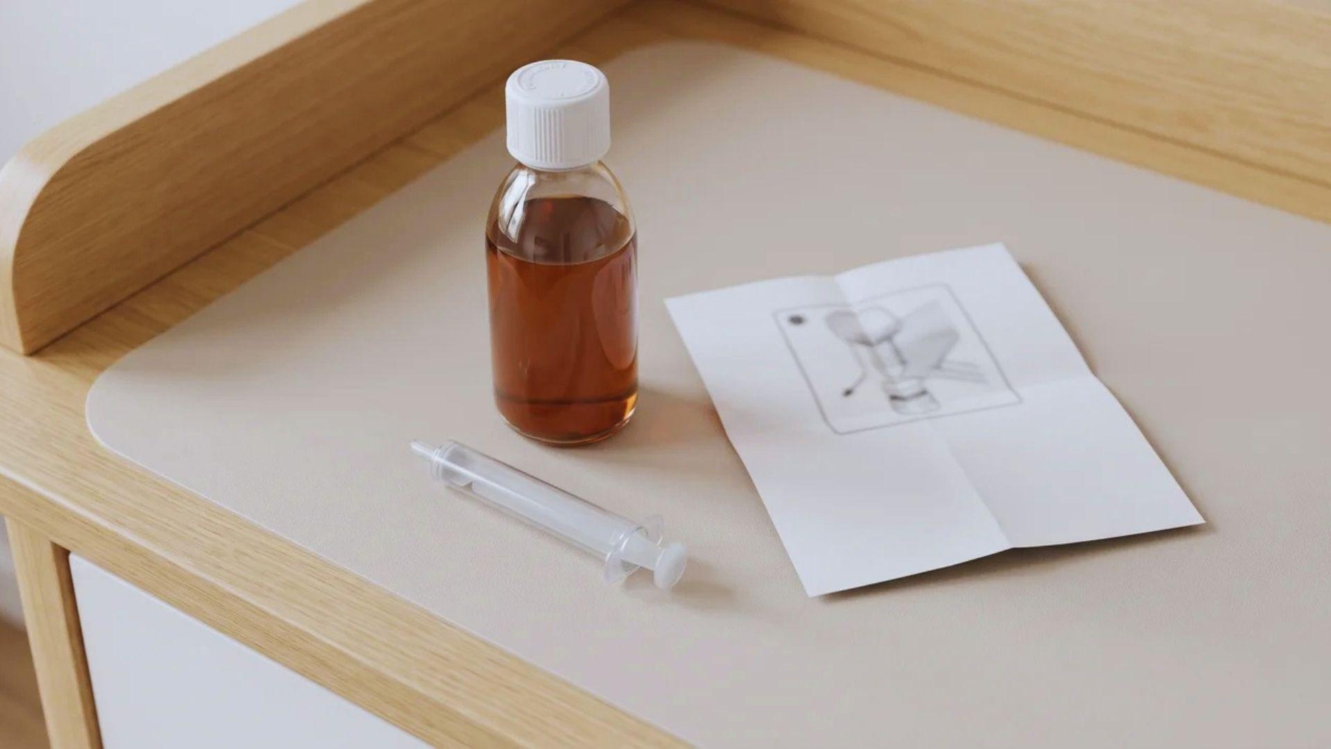 Infant acetaminophen bottle and oral dosing syringe on a nursery dresser.