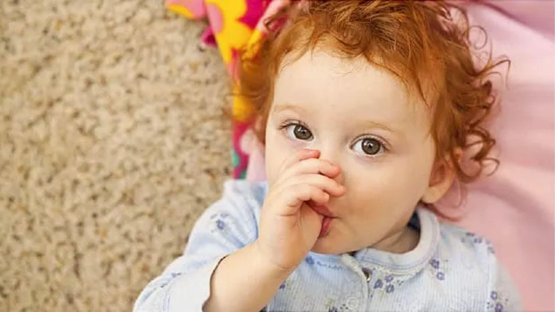 Curly red-haired baby lying down sucking thumb.