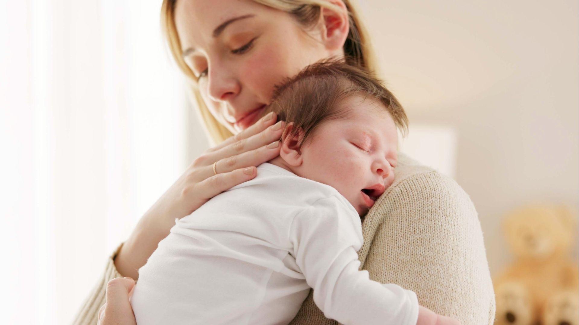 A mother gently cradles her sleeping newborn baby close to her chest.