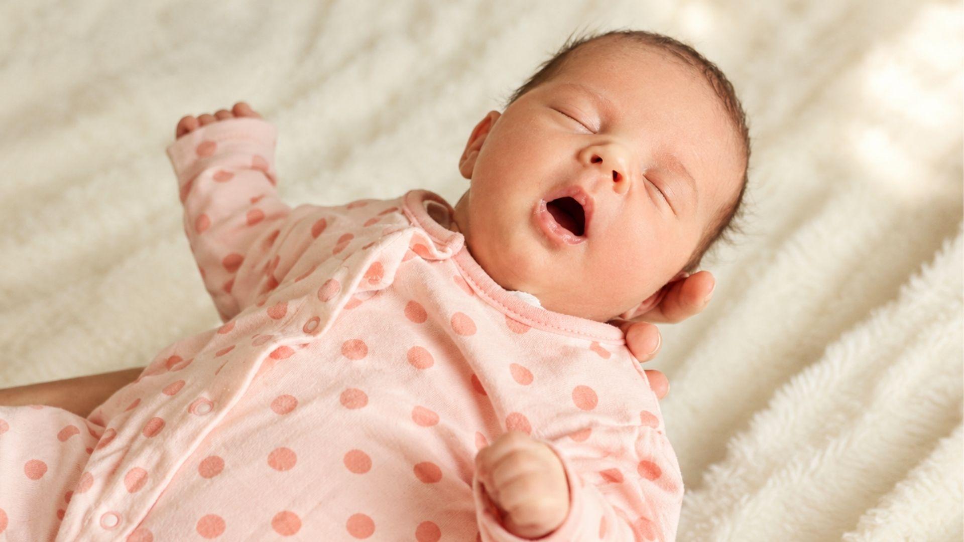 Newborn baby in pink polka-dot pajamas yawning.