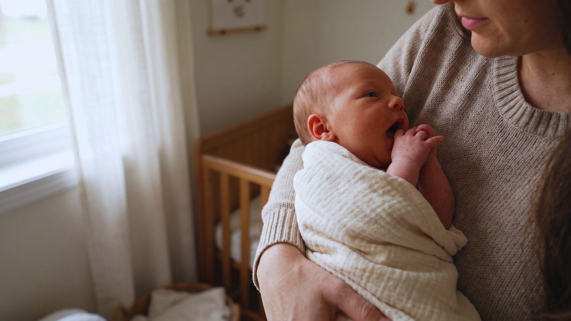 Parent holding a newborn showing hunger cues, with the baby’s mouth open and hand near the lips.