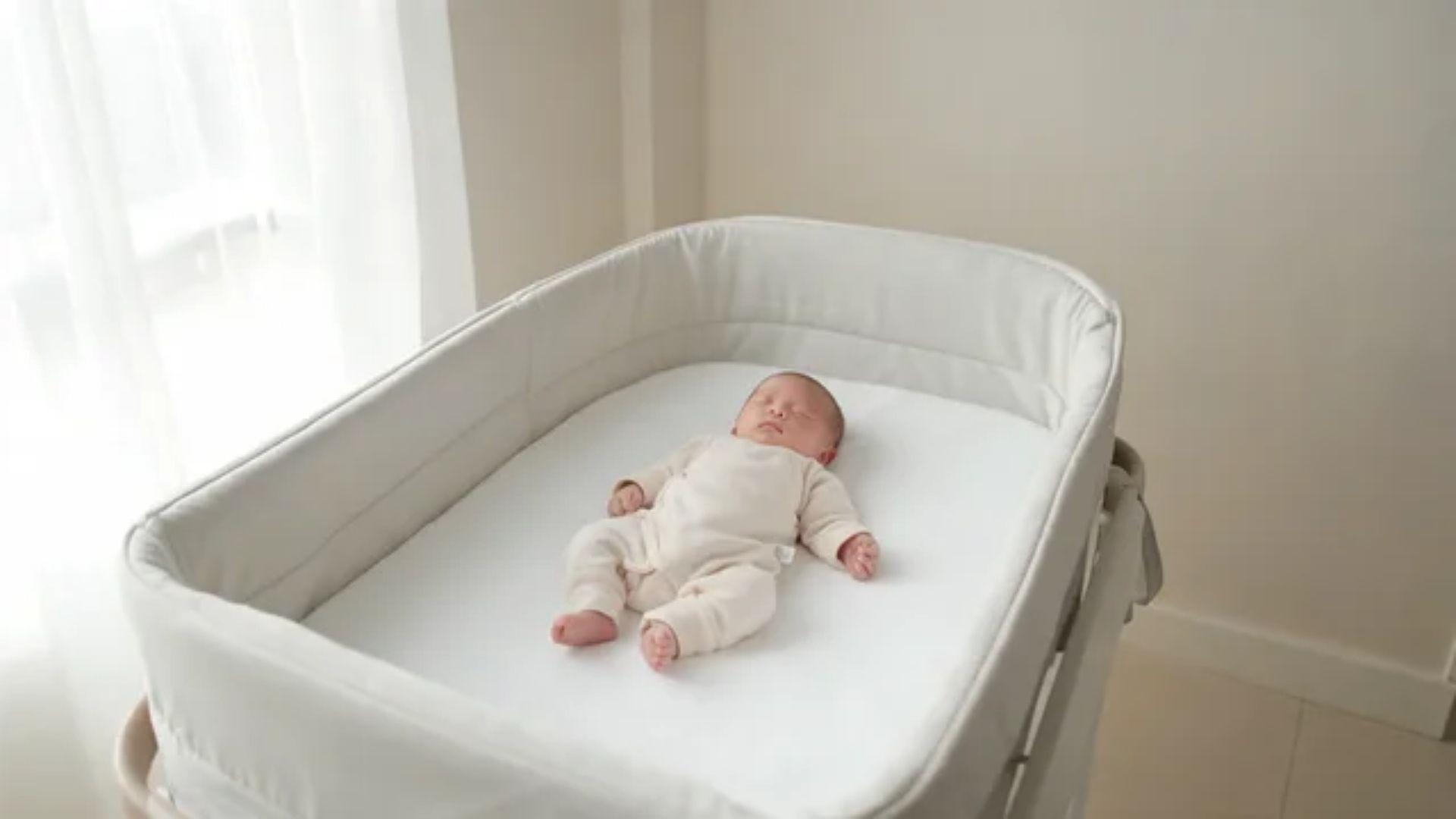 Newborn sleeping on their back in a bassinet with a firm mattress and fitted sheet