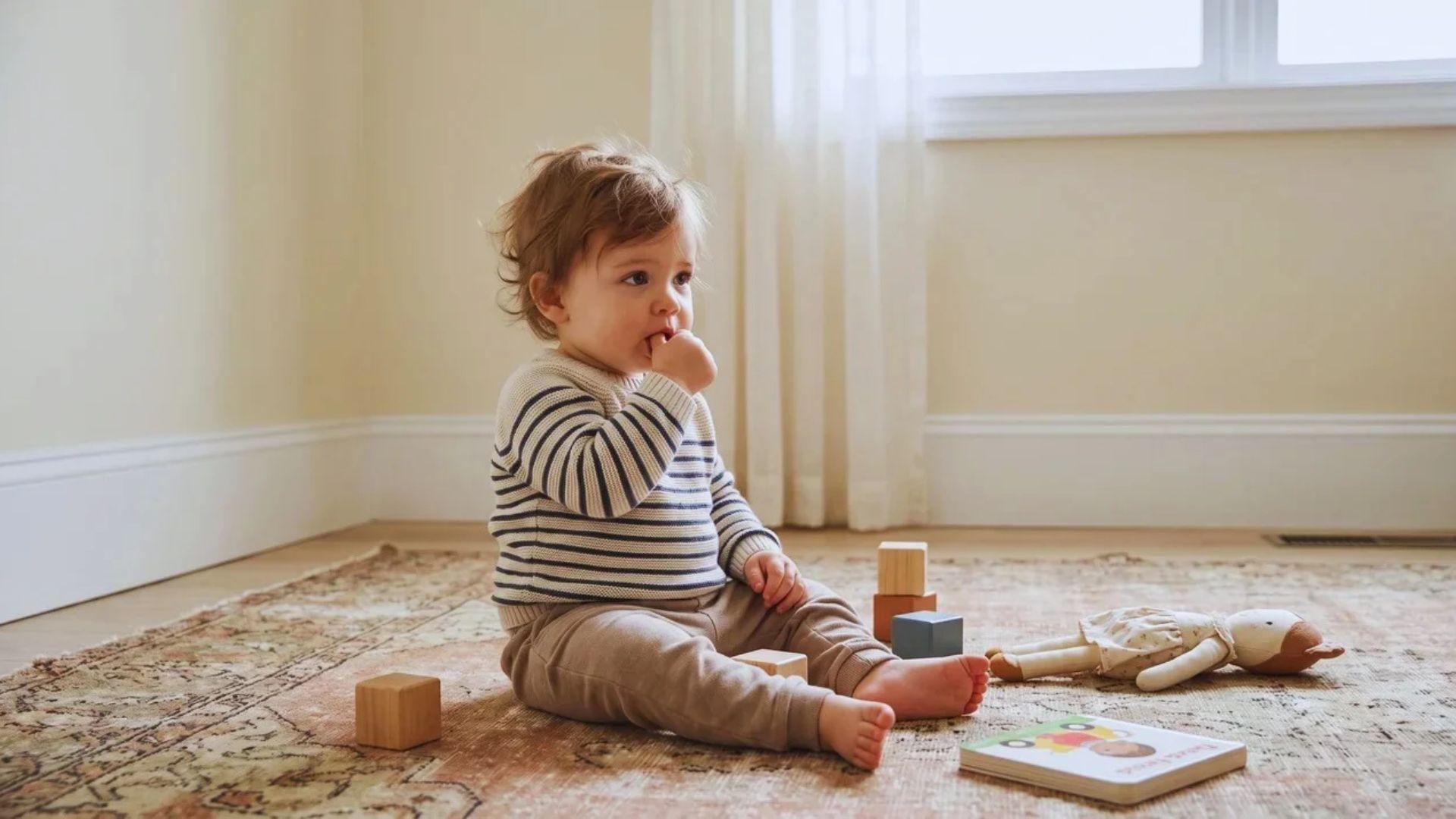 Young child sucking a thumb while sitting quietly in a home play area.
