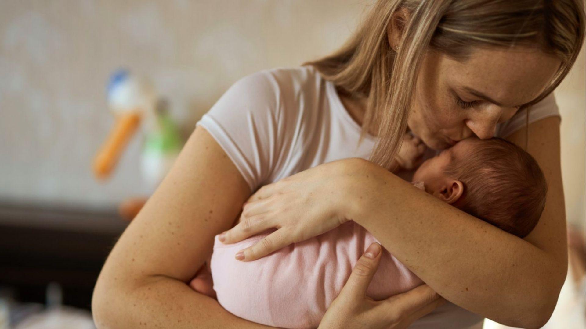 Mother kissing newborn’s forehead while holding close.
