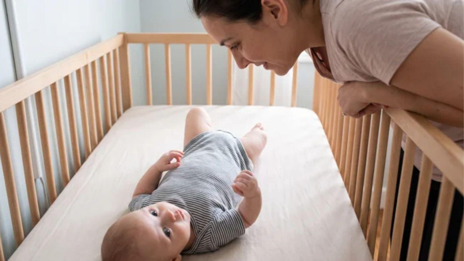 Parent watching an alert baby lying on their back in a bare crib