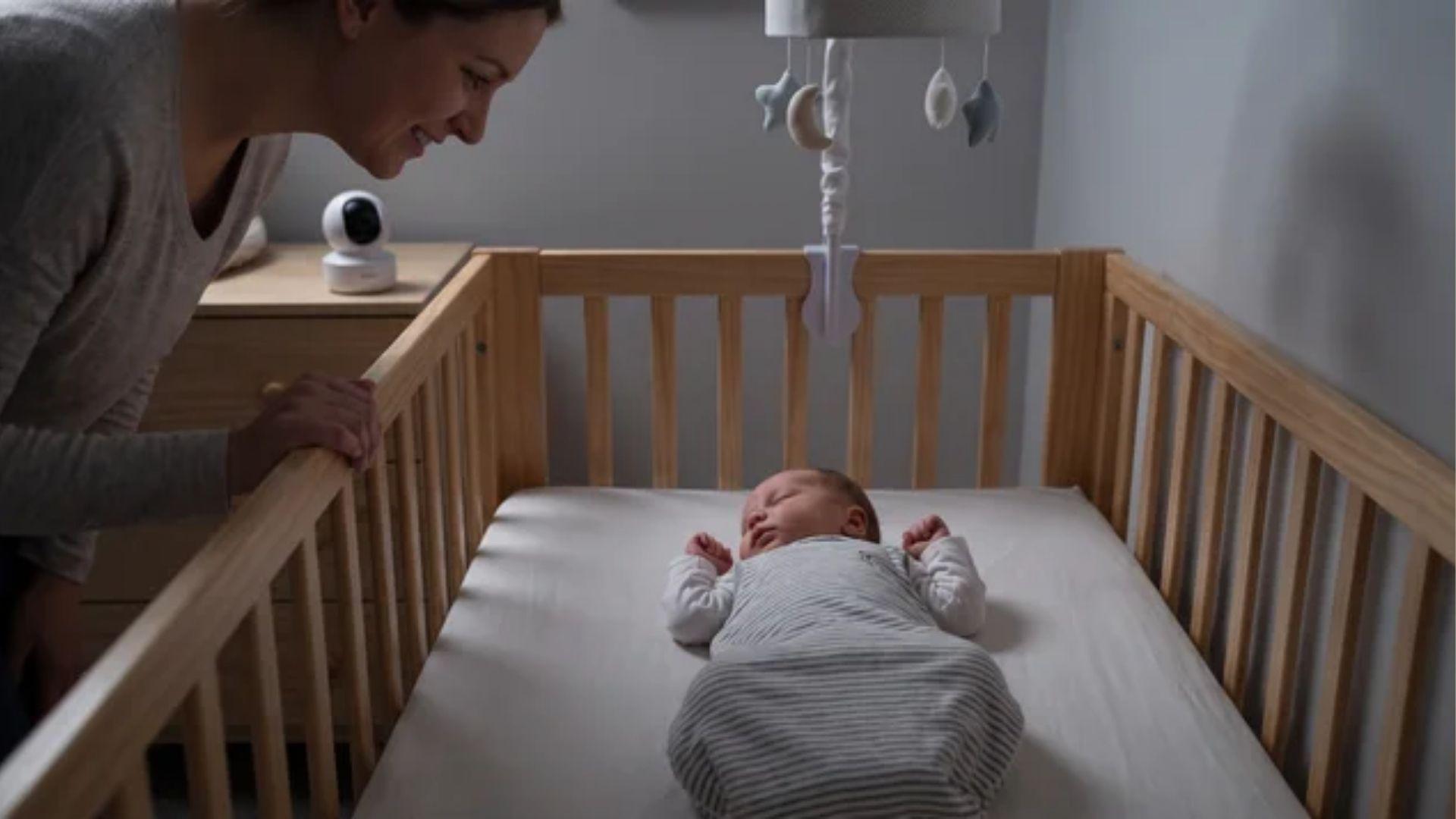 Parent watching sleeping baby in crib, observing normal sleep behavior in a newborn