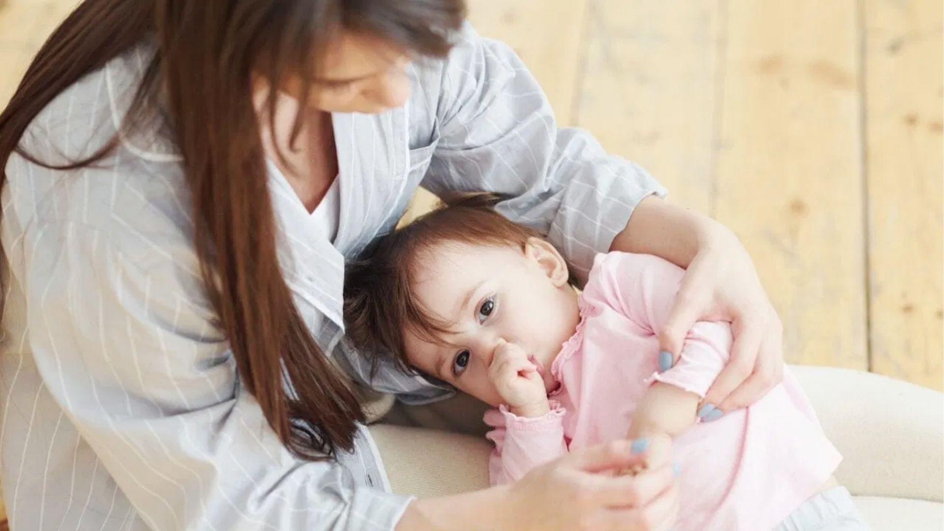Mother cuddling toddler who sucks thumb on couch