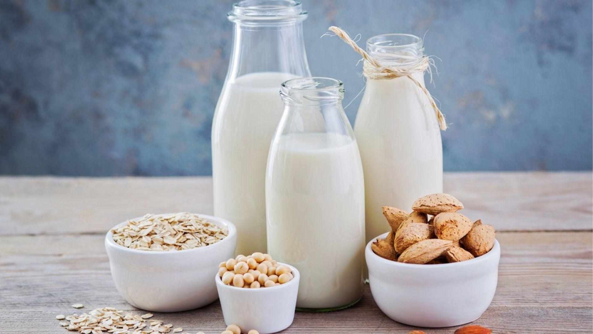 Glass bottles of plant-based milk with bowls of oats, soybeans and almonds.