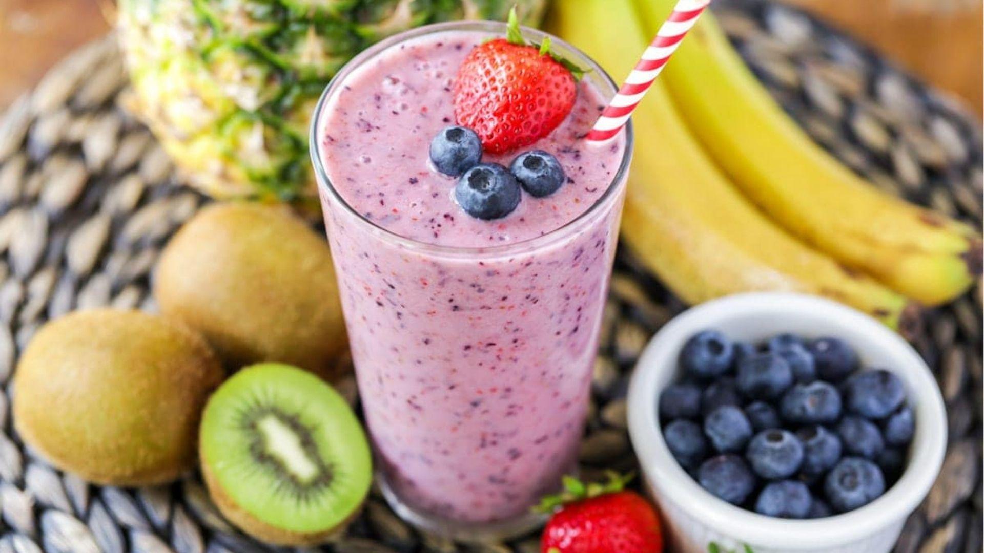 Berry smoothie topped with blueberries and strawberry surrounded by kiwi banana pineapple for kids.