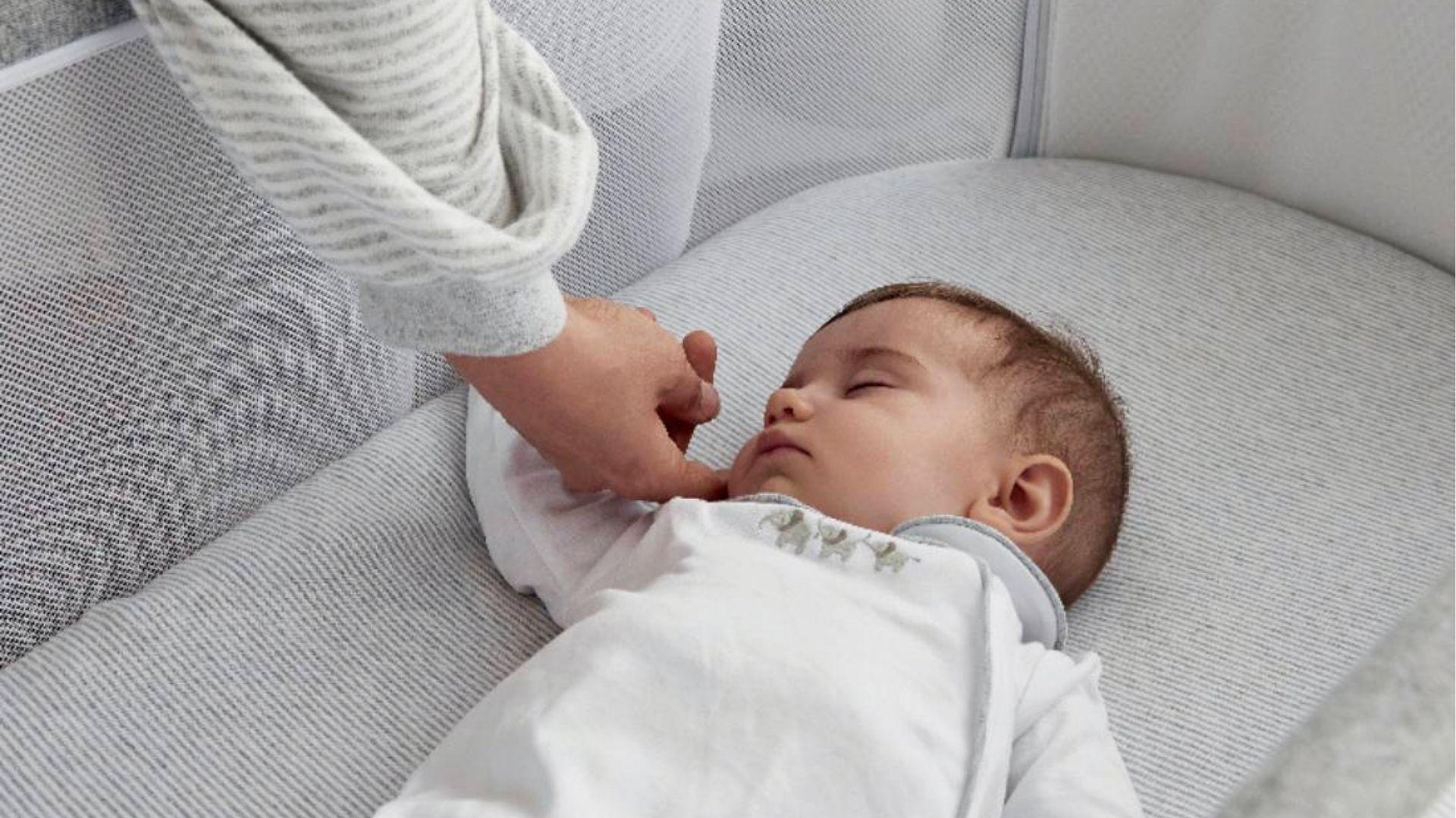 Sleeping baby lying on a crib mattress with an adult touching the baby's face