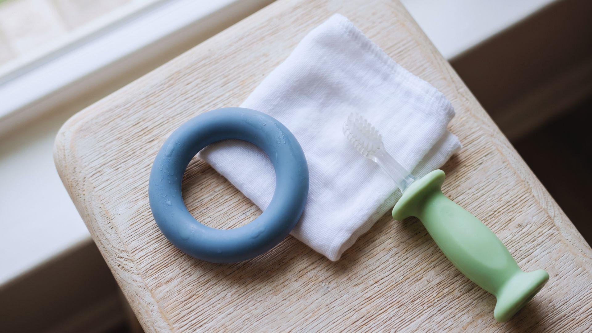 Silicone teether, damp washcloth, and soft baby toothbrush arranged on a surface.