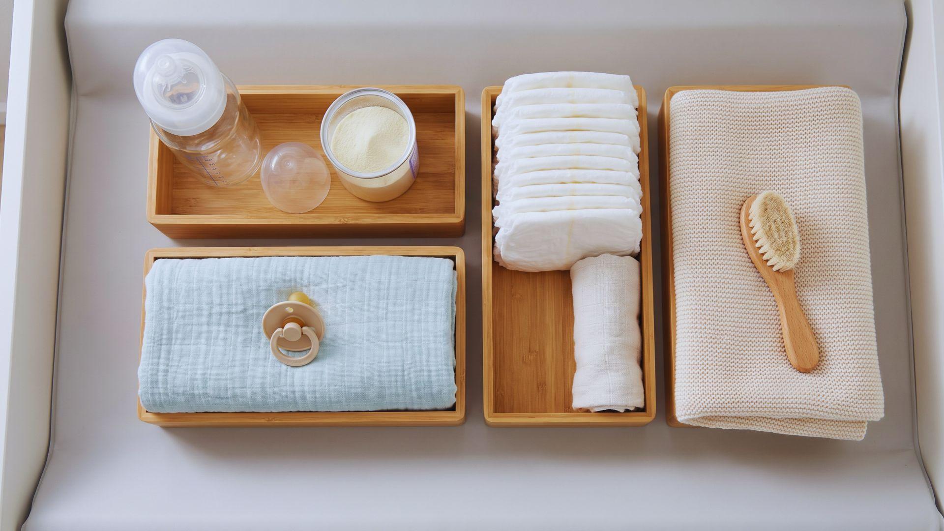 Feeding bottle, swaddle blanket, pacifier, diaper, burp cloth, and baby blanket arranged on a nursery surface.