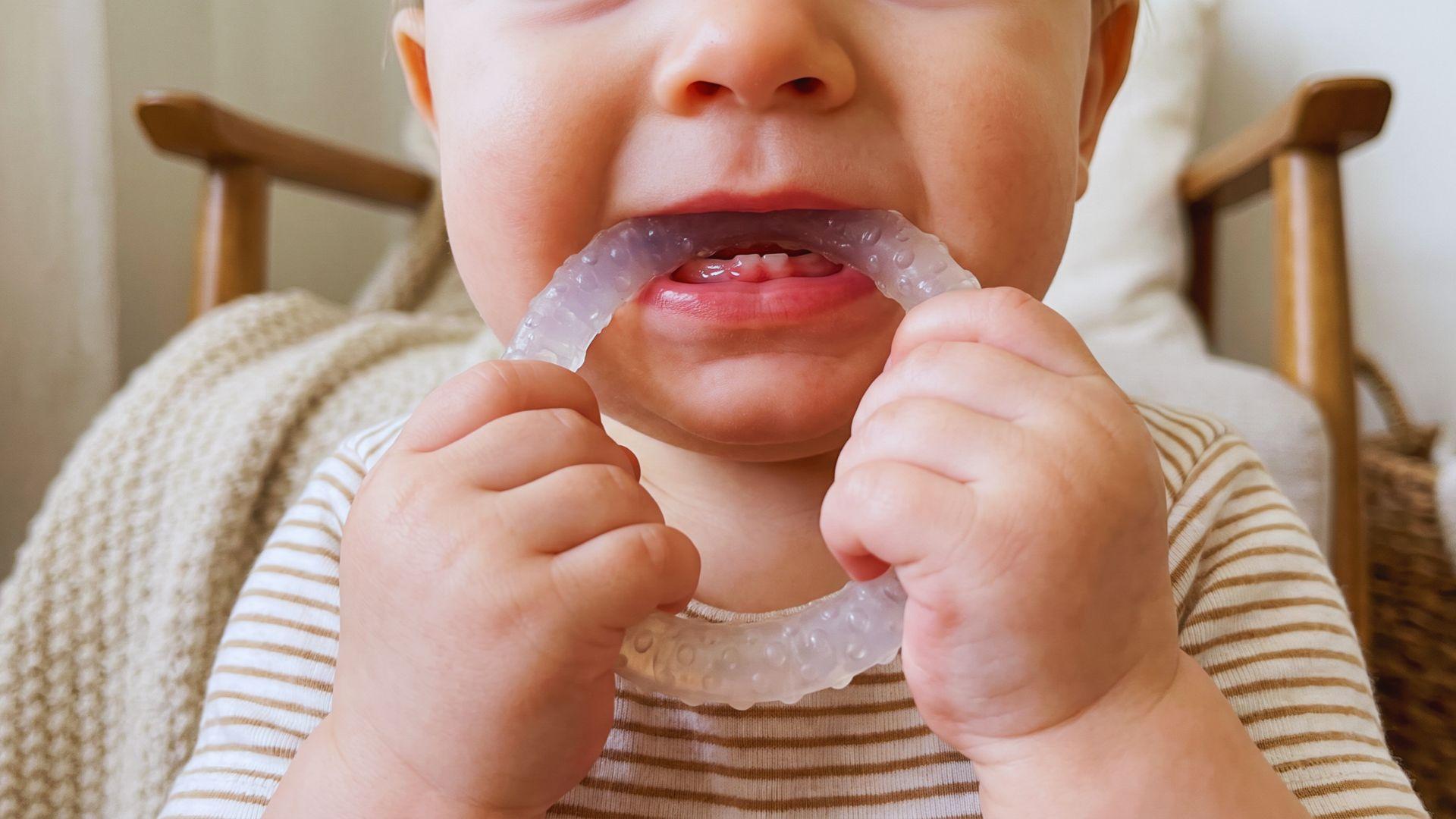 Baby chewing a silicone teether with mild swelling visible along the lower gums