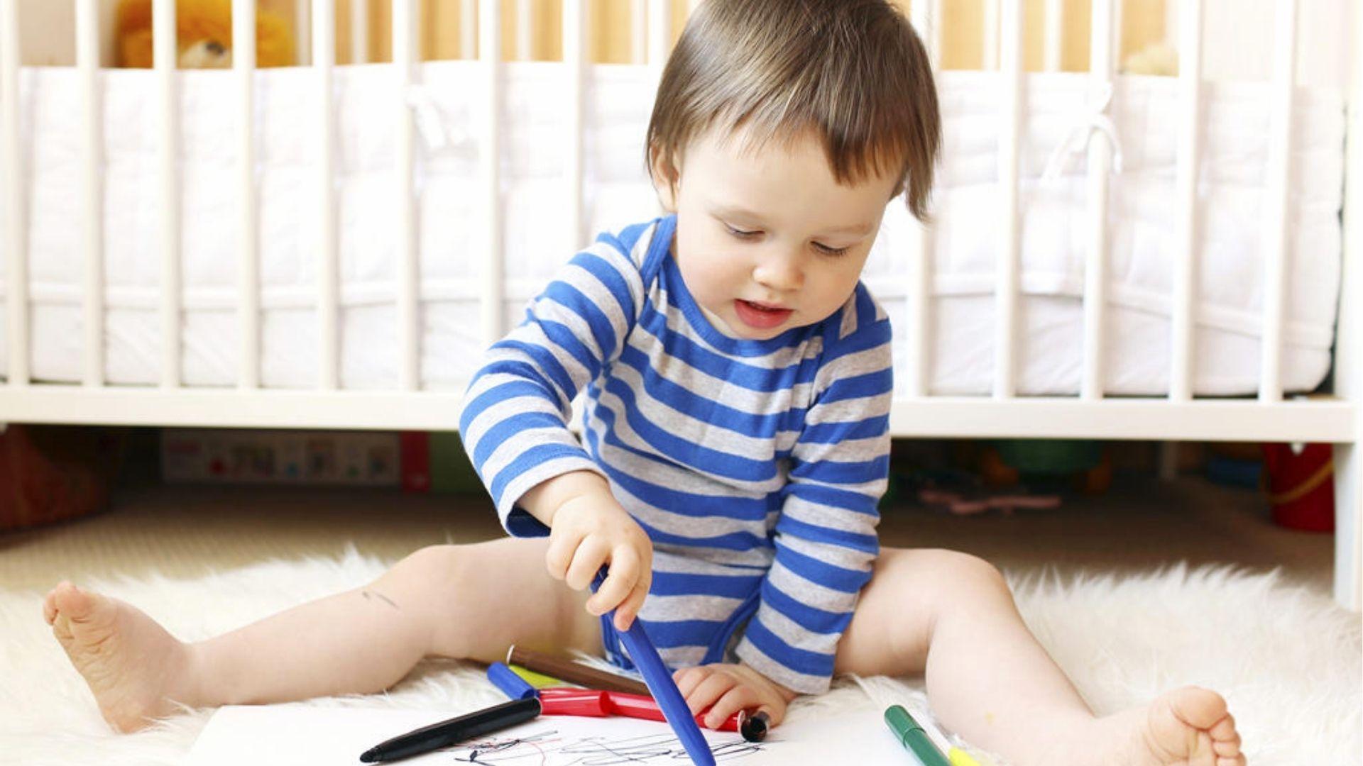 Toddler in stripes scribbling with markers, learning to speak.