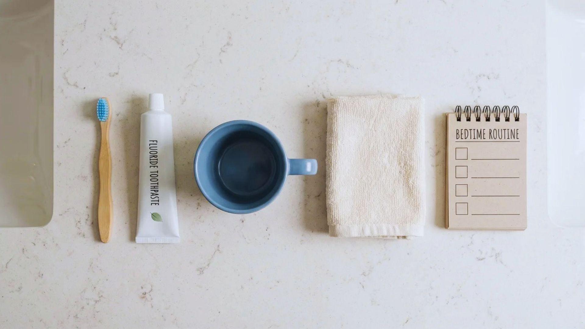 Children's toothbrush, toothpaste, cup, and folded washcloth arranged for a bedtime routine.