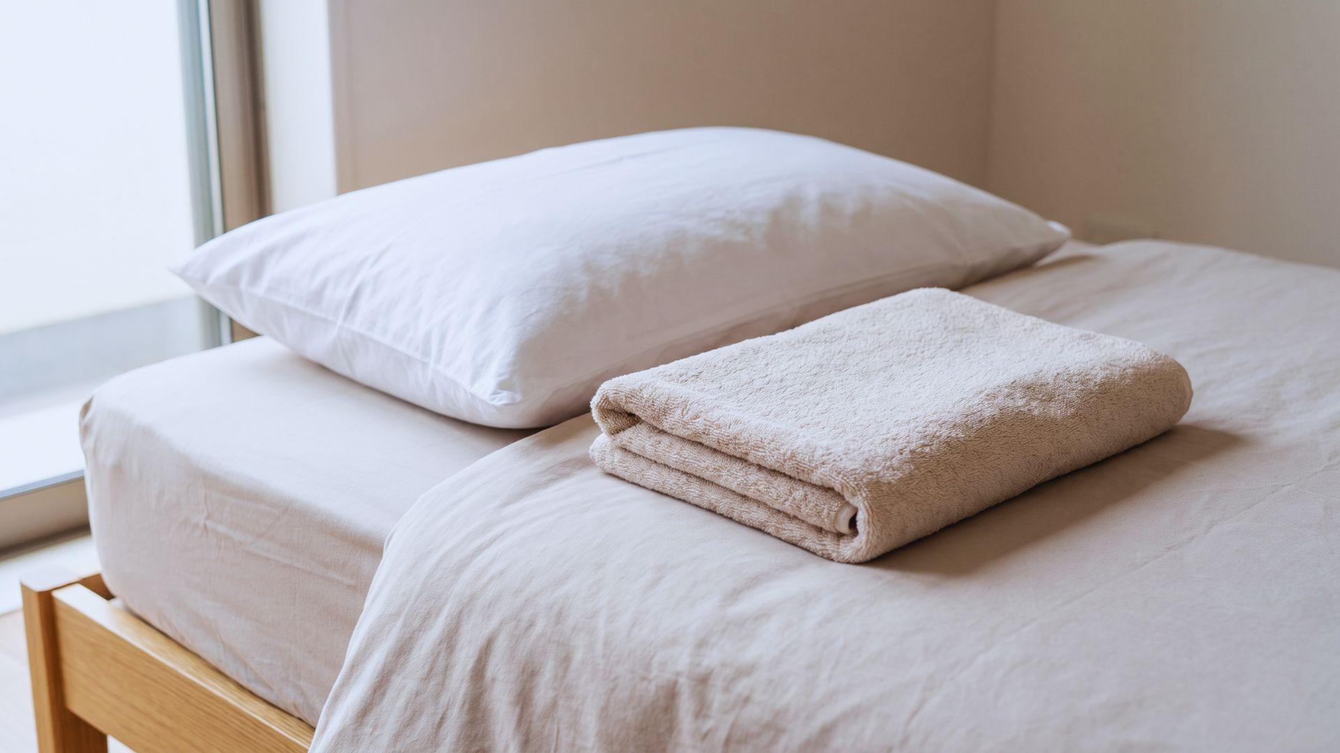 Pillow and folded towel arranged on a flat bed surface for a toothbrushing setup.