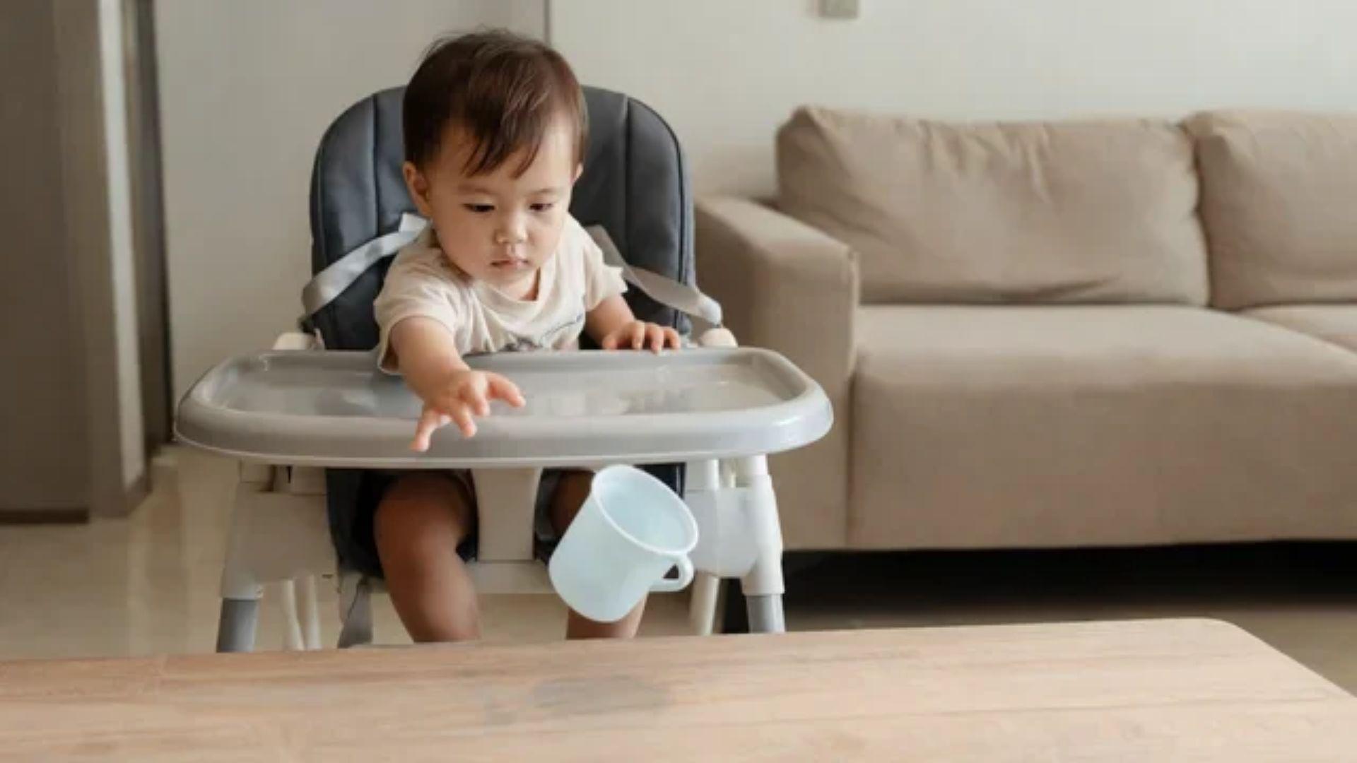 Toddler in a highchair dropping a cup toward the floor