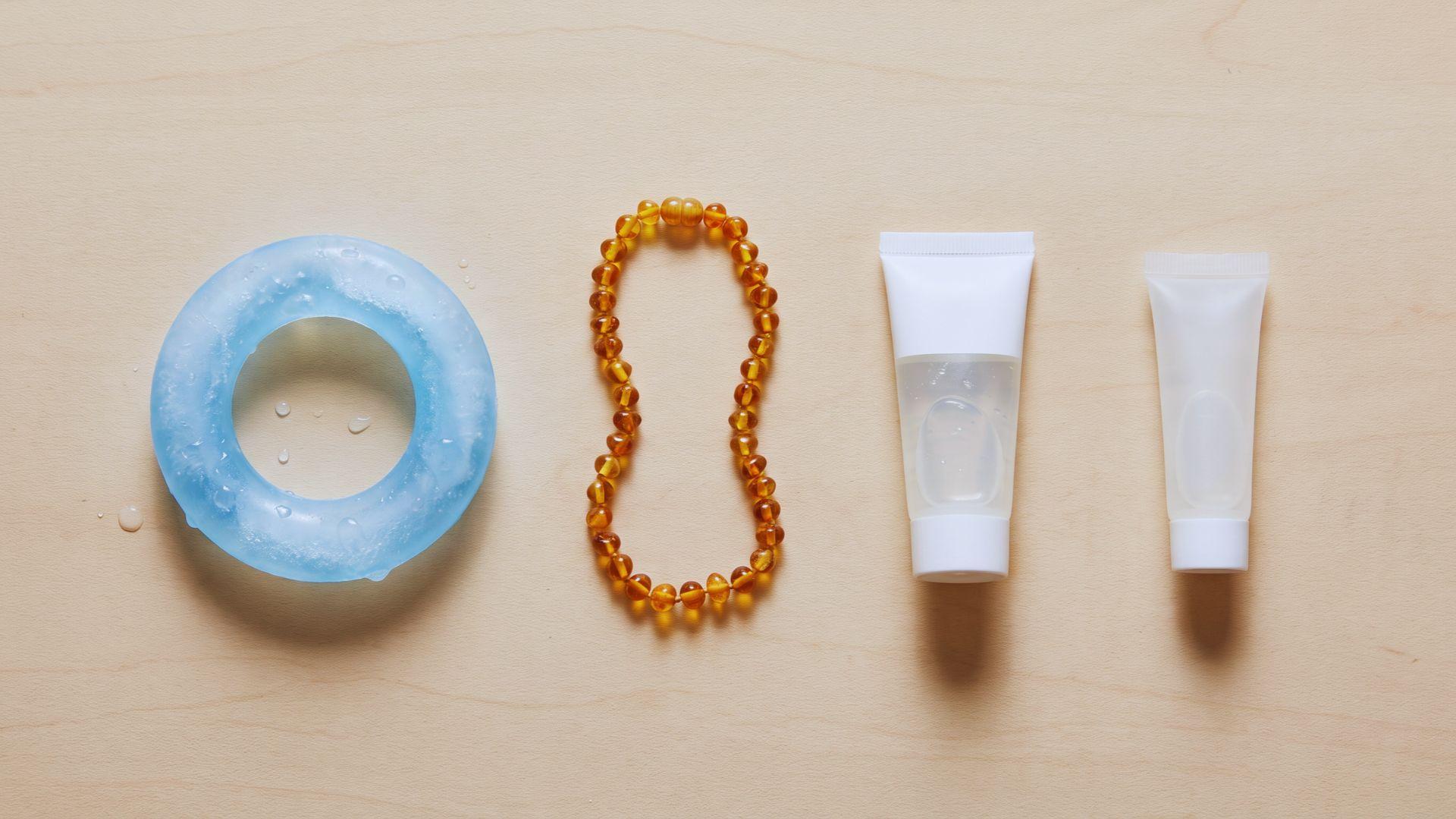 Frozen teething ring, amber necklace, and two unbranded oral gel tubes on a tabletop.