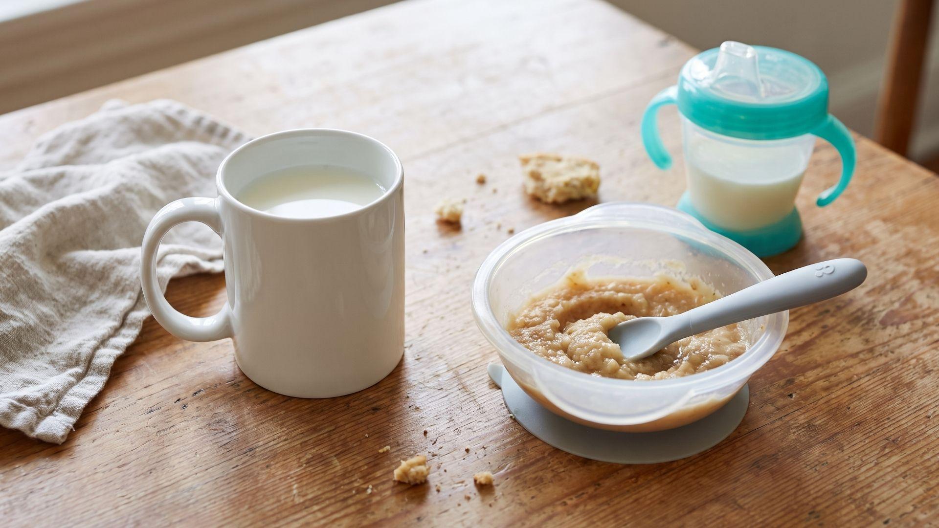 Whole pasteurized cow's milk in a cup beside toddler feeding items