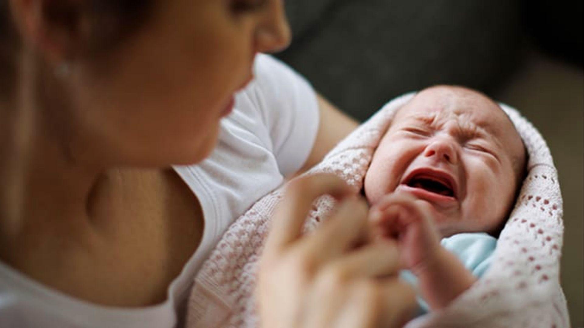 Mother holds crying newborn wrapped in blanket, trying to soothe baby’s distress.