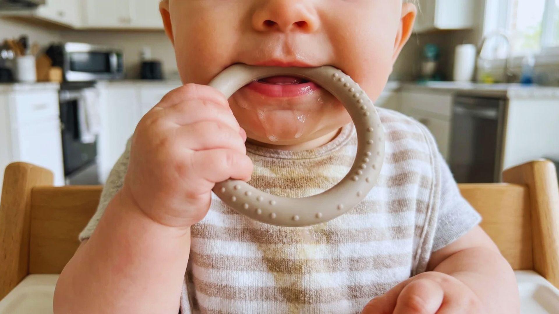 Baby mouthing a teething toy with saliva visible around the mouth.