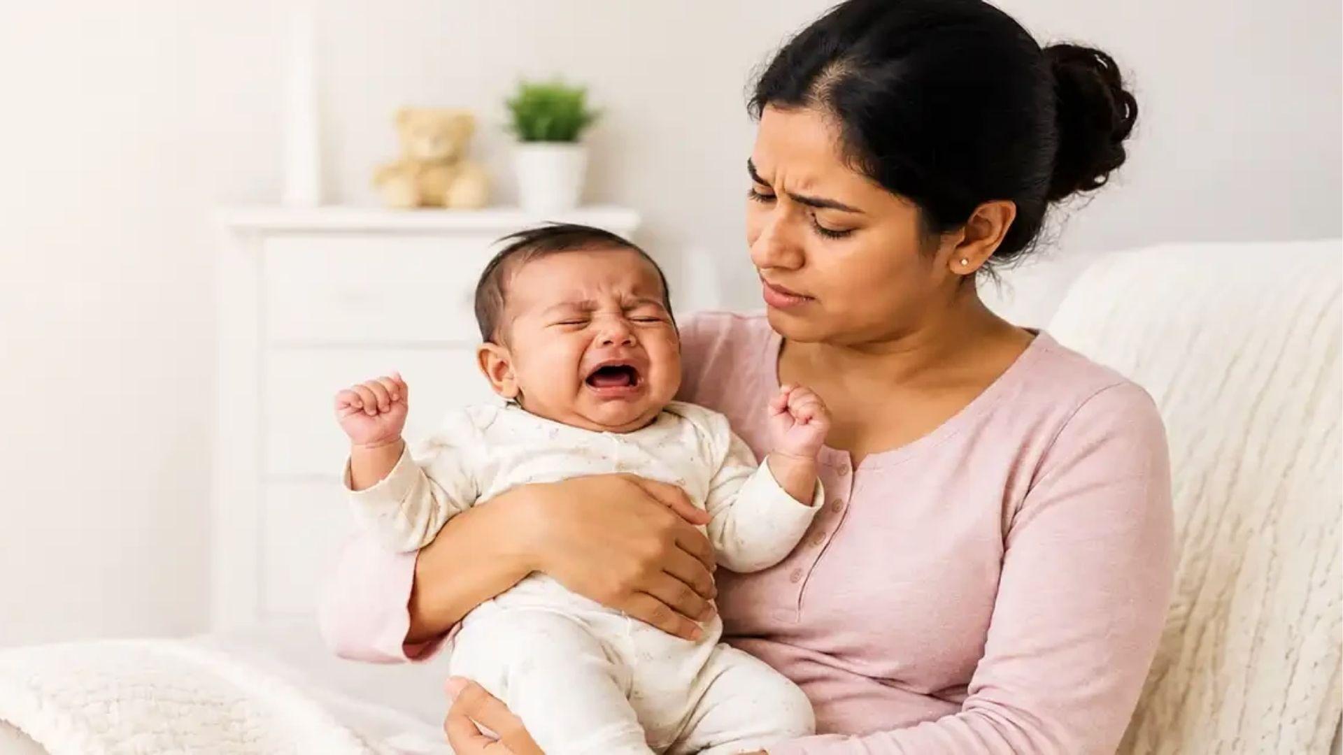 Worried mother holds wailing infant on lap, showing stress of frequent crying.